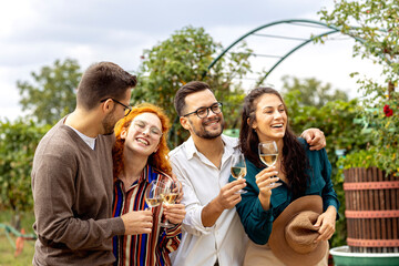 Four friends in vineyard talk to each other and smile with glass of vine in hands