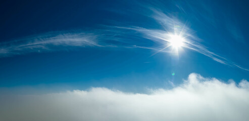 Aerial photo above clouds with Sun, clear sky above fast moving white cloudscape