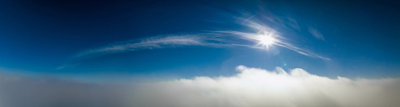 Wide panorama Aerial photo above clouds with Sun, clear sky above fast moving white cloudscape