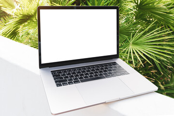 laptop mockup. Notebook with white screen with palm tree leafs on background. Vacation, traveling and remote work and study concept. Empty copy space, blank screen modern laptop.