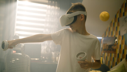 Excited teenage boy with VR headset and holds joysticks. Young boy uses virtual reality headset and plays games in his room.