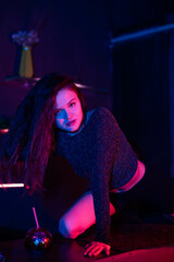 Hot woman looking at camera while standing on table. A smile on her face . Brown long curly hair falling over her shoulders. Kneeling on the cocktail table.