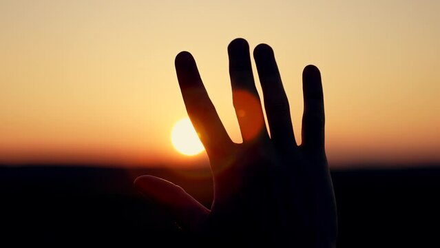 Light backdrop. Sunlight sky. Silhouette of palm of hand at sunset close-up. Man stretches his hand to sun silhouette. man's hand in sun close-up. concept of dreams, religion, motivation