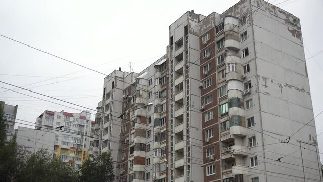 Large high soviet building panoramic view from bottom to top. An old dilapidated house from the times of the USSR. Concrete panel building against the background of gray clouds.
