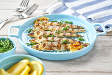 Baked sardines with rosemary and lemon in a blue bowl, on a white table, selective focus.