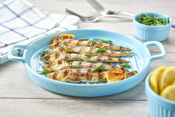 Grilled sardines with salt, herbs and lemon slices on a white table, selective focus.