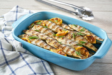 Roasted fish with rosemary and lemon in a blue square baking tray, selective focus.