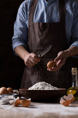 Man chef breaking egg holding knife at flour for bread or pastry making. Bakery concept