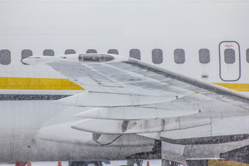 Wing of a white passenger jet airliner in winter. Photo from the side. The plane is taxiing for takeoff. Aviation lights.