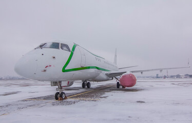 A jet passenger plane stands parked at the airport with covers put on engines in winter against a cloudy sky
