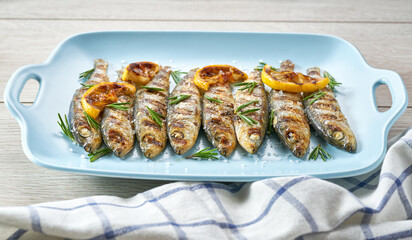 Grilled sardines with salt, herbs and lemon slices on a white table, selective focus.