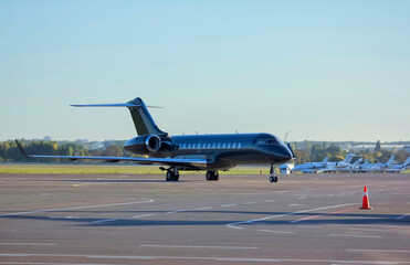 A dark green private business jet is parked at the airport in front of other business jets, no tail numbers
