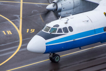 A propeller-driven white-and-blue Soviet plane rides along the taxiway at the airport, close-up top view
