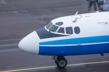 A propeller-driven white-and-blue Soviet plane rides along the taxiway at the airport, close-up top view

