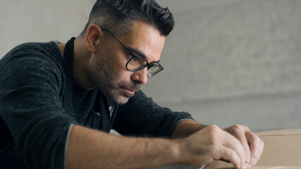 Obraz premium Experienced ceramist with an apron uses sculpting tool with both hands to create the design details on the sculpture of a prototype, eco friendly model of a car made of raw clay.