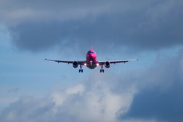 A white and pink jet passenger airliner comes in for landing against a clear sky. Low angle photo from the end of the runway