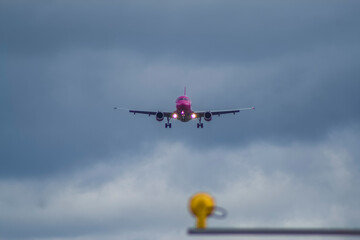 A white and pink jet passenger airliner comes in for landing against a clear sky. Low angle photo from the end of the runway