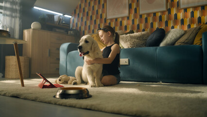 Young girl playing with dog with toy and ball, sitting on mild carpet, feeding puppy, talking and having fun with pet, spending leisure time at home. Golden retriever.