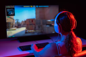 Rear view of a caucasian woman playing a computer game in neon light in the dark.