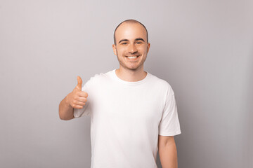 Ecstatic young bald man is holding thumb up and smiling to the camera.