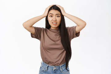 Oh my gosh. Shocked and worried asian woman, looking concerned and anxious, panicking, standing over white background