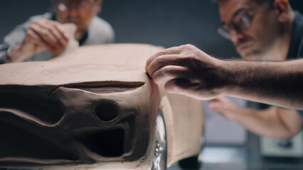 Two male automotive designers creating futuristic plasticine clay prototype of car with...