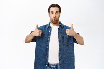 Handsome smiling bearded man, shows thumbs up, approve smth, recommending product, praise or...