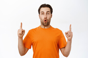 Impressed man points up, shows smth on top, making impressed face expression, standing over white...