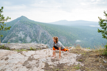 The guy does stretching of muscles and ligaments standing in nature in the mountains, yoga practice on a rock, lunge in front, fitness in the morning with a beautiful view, workout
