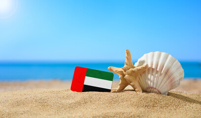 Fototapeta na wymiar Tropical beach with seashells and UAE flag. The concept of a paradise vacation on the beaches of the United Arab Emirates.