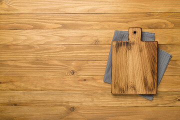 Cutting board with towel on wooden background, top view