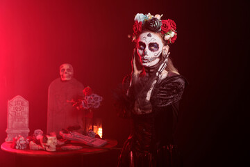 Santa muerte showing kissy face in studio, posing and looking flirty in goddess of death traditional costume. Creepy model acting like la cavalera catrina on holy day of the dead ritual.