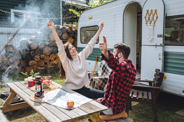 Young beautiful loving couple travelling across country in the van. Millennial man and woman in a travel camper. Cozy atmosphere, vacations vibe. Drinking tea, choosing new destination on a map