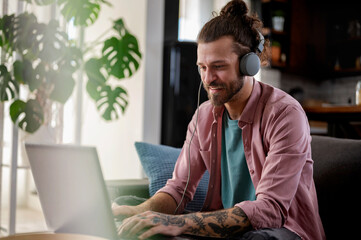 Young cheerful man with a sleeve tattoo using laptop computer. Freelance entrepreneur working from home