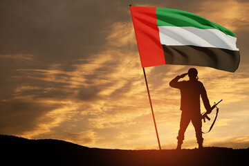 Silhouette of soldier saluting with the flag of UAE against sunset or sunrise. Concept of national...
