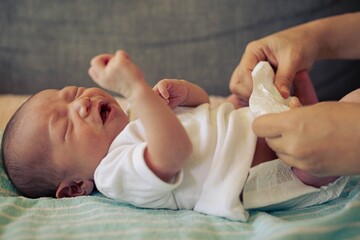 A mother changing her newborn baby’s diaper at home. Parents caring for infants.