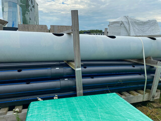 Large plastic pipes of large diameter with flanges in an open-air storage warehouse for the storage...