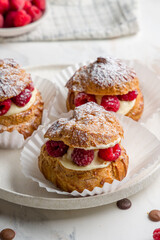 profiteroles with cream and fresh raspberries on white plate on white marble table vertical