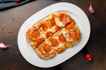 Pepperoni pizza on Roman dough pinsa top view on brown dark table