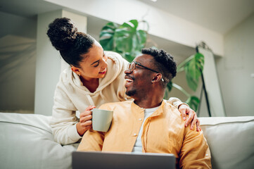 Multiracial couple using laptop while sitting on a sofa at home