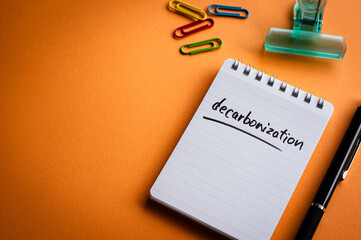 There is a notebook with the word decarbonization. It's placed on a color background.