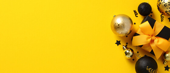 Black Christmas gift box with yellow ribbon bow, balls, confetti on yellow background. Xmas banner...