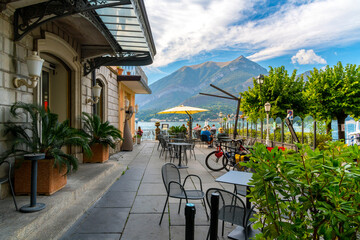 Tourists dine at a waterfront outdoor cafe along the shores of Lake Como at summer in the picturesque town of Bellagio, Italy.