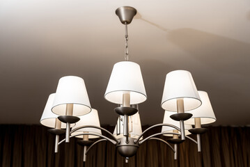 A round chandelier of several lamps against a light ceiling, full frame, side view
