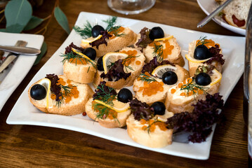 a lot of sandwiches with caviar, olives and lemon on a white plate