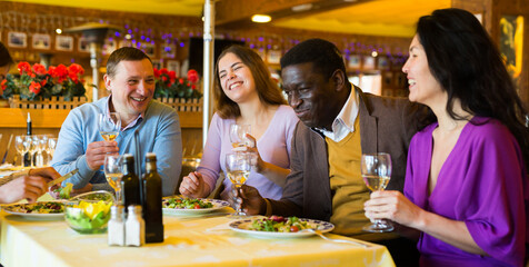 Cheerful adult people of different nationalities enjoying evening meal in restaurant. Friendly...