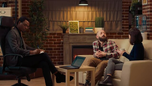 Displeased couple attending counseling session with therapist to solve relationship problems and conflict. Man and woman complaining about marriage, asking for assistance. Tripod shot.