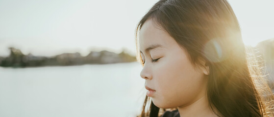 Preteen mixed girl meditating with eyes closed by lake, child positive mental health, peace and...