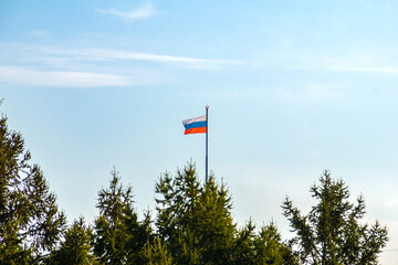 the Russian flag is visible above the coniferous forest on a flagpole with a warning red signal lamp, selective focus