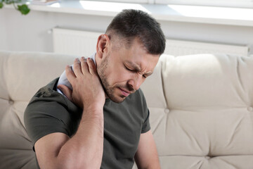 Fototapeta premium Man using heating pad on sofa at home